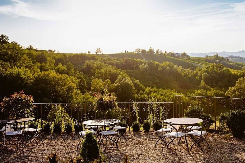 A long, unhurried lunch on a sunlit terrace overlooking rolling vineyards in Piedmont, Italy, with glasses of red wine, sharing plates, and green hills fading into the distance.